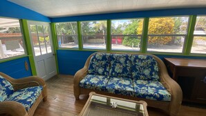 A room with a blue and green color scheme, featuring a wicker sofa with a floral cushion, a matching armchair, and a glass-top coffee table.