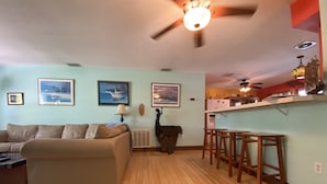 A living room with a sofa, a dining area with stools, and a kitchen with a countertop.