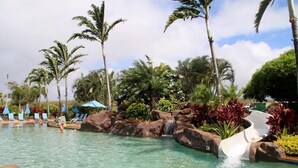 Un espace piscine avec une eau claire, des palmiers et un toboggan aquatique.