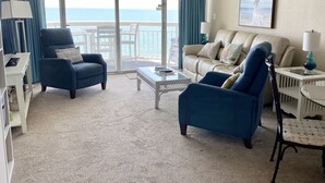 Ein Wohnzimmer mit einer Couch, Sesseln, einem Couchtisch und Meerblick durch große Glasfenster.