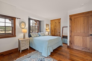 A bedroom with a bed, nightstands, a wooden wardrobe, a large window, and a door.