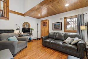 A living room with a wooden ceiling, a grey sofa, a brown leather sofa, a wooden door, and a window with curtains. - Quiet, Comfy & Spacious: Cabin within 10 mi of Mt. Rushmore & Custer State Park (Keystone)