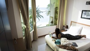 Een hotelkamer met een bed, een laptop en uitzicht op de oceaan.