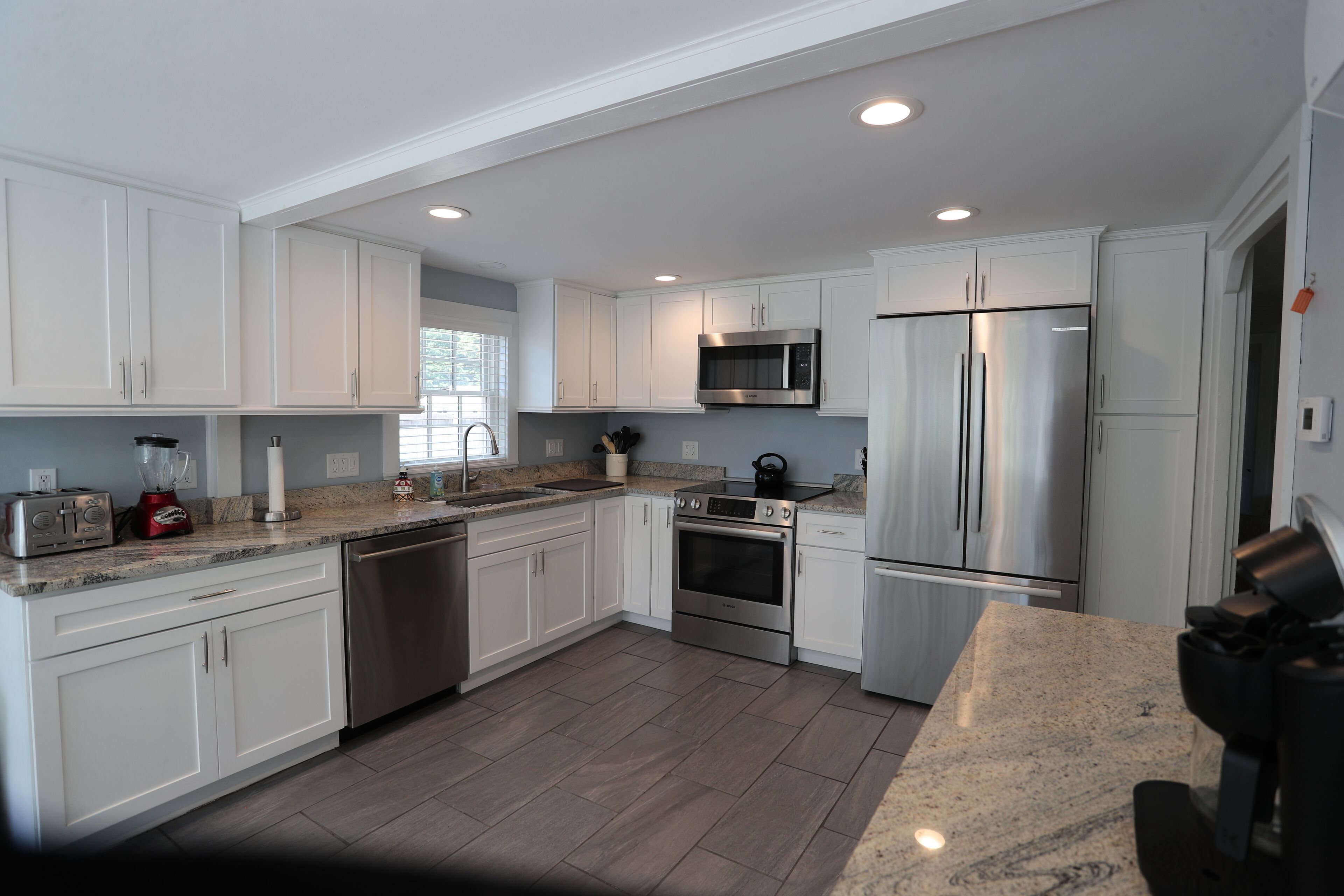 A modern kitchen with white cabinets, stainless steel appliances, granite countertops, and a dishwasher.