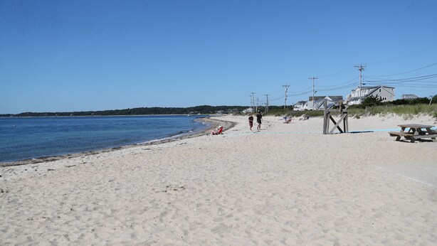 Une plage de sable avec une jetée en bois, une table de pique-nique et un poste de surveillance pour les sauveteurs.