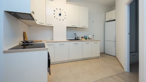 A modern kitchen with white cabinets, a black clock, a sink, and a stove. - ShortStayPoland Środkowa - B49 (Warsaw)