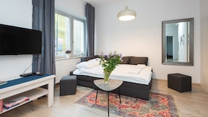 A modern bedroom with a bed, bedside table, TV, and a window with curtains. - ShortStayPoland Środkowa - B49 (Warsaw)
