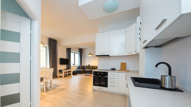 A modern kitchen with white cabinets, a built-in oven, and a black sink. - ShortStayPoland Środkowa - B49 (Warsaw)
