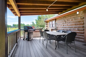 A covered outdoor deck with a grill, a table, and chairs. - SPECIAL RATES Pet Friendly Log Cabin, Sleeps 8, Hot Tub, Fishing & Skiing Galore (Manhattan)