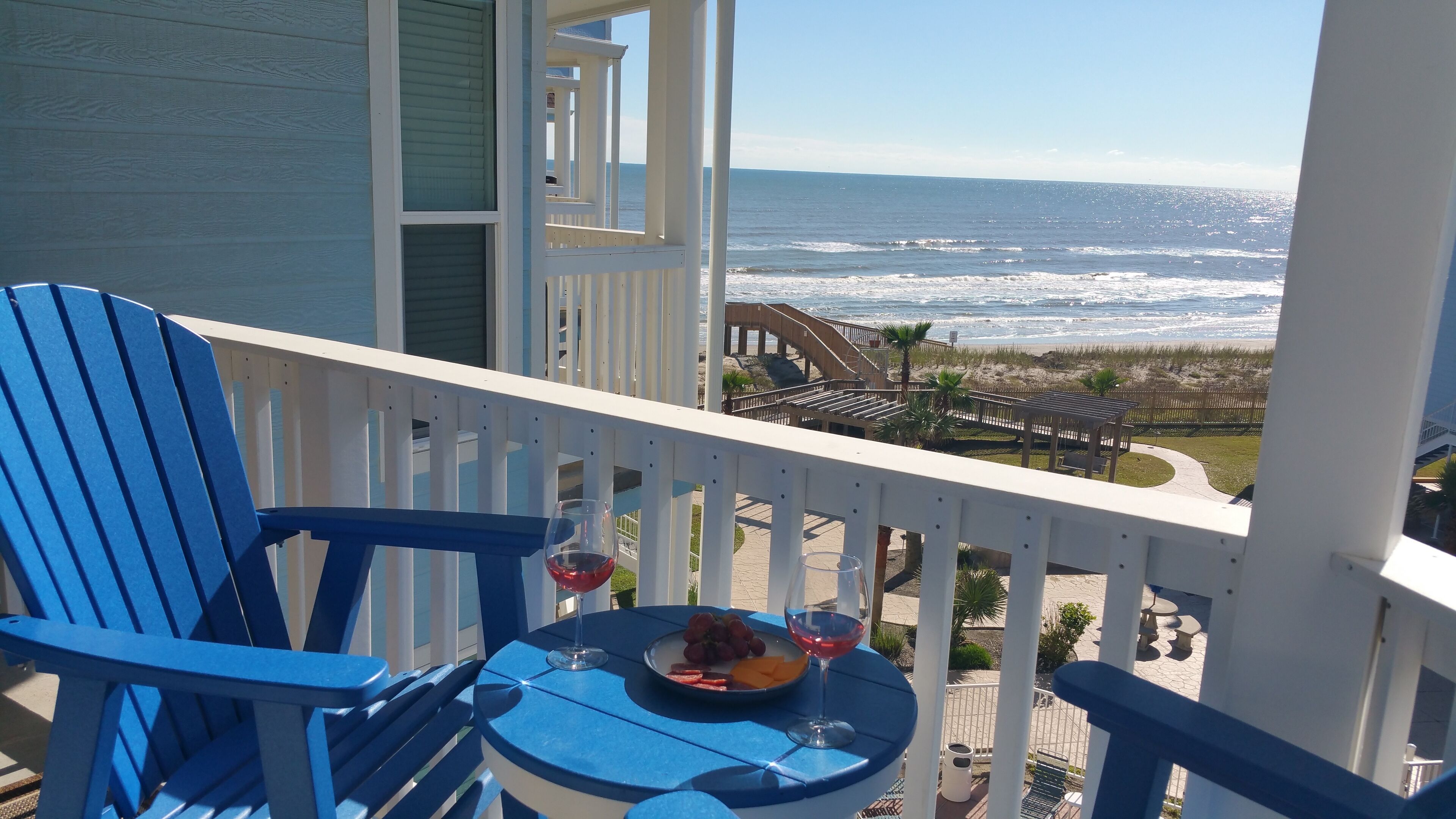 Een balkon met blauwe stoelen en een tafel, gedekt met fruit en twee wijnglazen.