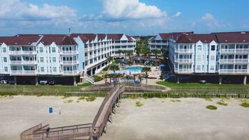 A beachfront hotel with multiple balconies, a swimming pool, and a boardwalk leading to the beach.