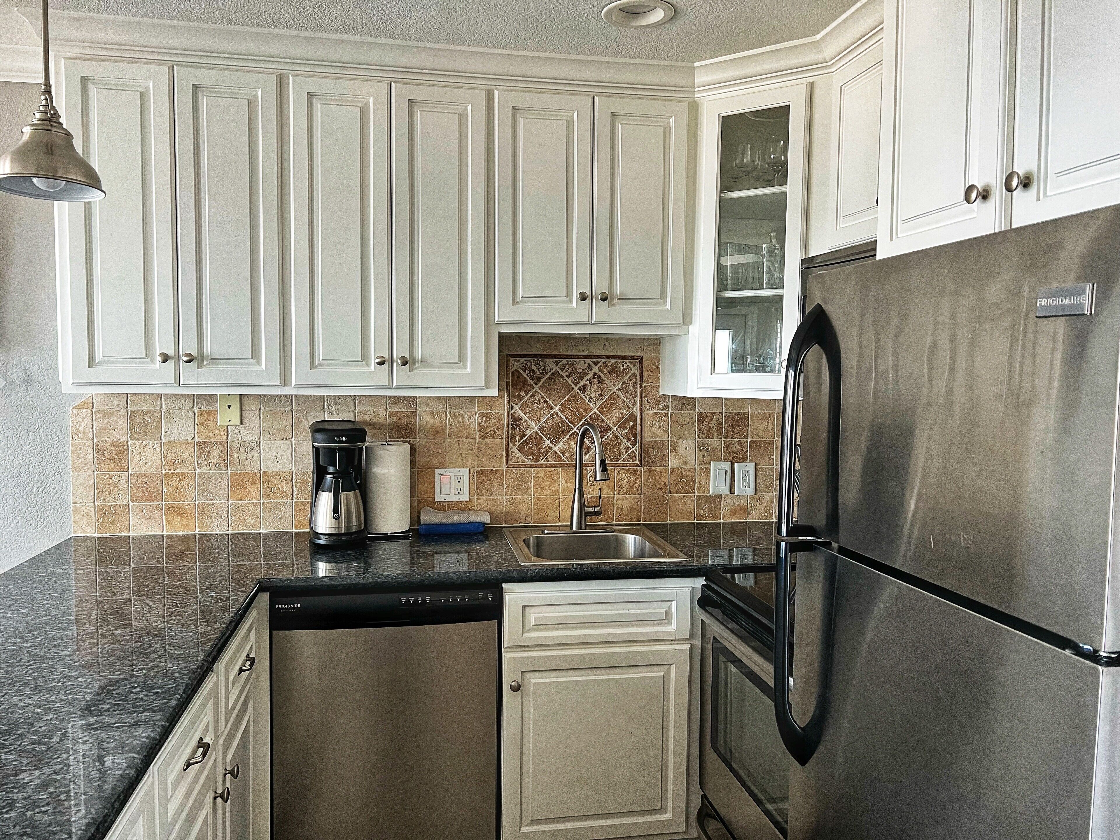 A kitchen with white cabinets, a stainless steel refrigerator, a coffee maker, and a tiled backsplash.
