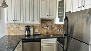 A kitchen with white cabinets, a stainless steel refrigerator, a coffee maker, and a tiled backsplash.