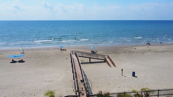 A beach with a wooden boardwalk leading to the water, umbrellas, and a few people.