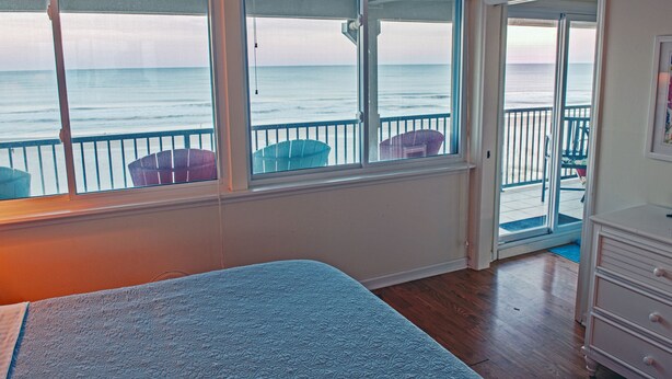 A bedroom with a large window overlooking the ocean, a bed, and a dresser.