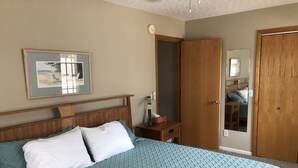 A bedroom with a bed, a nightstand, a wooden wardrobe, a mirror, and a framed picture on the wall.