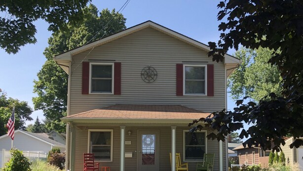 A two-story house with a front porch, a mailbox, and a small garden with chairs.