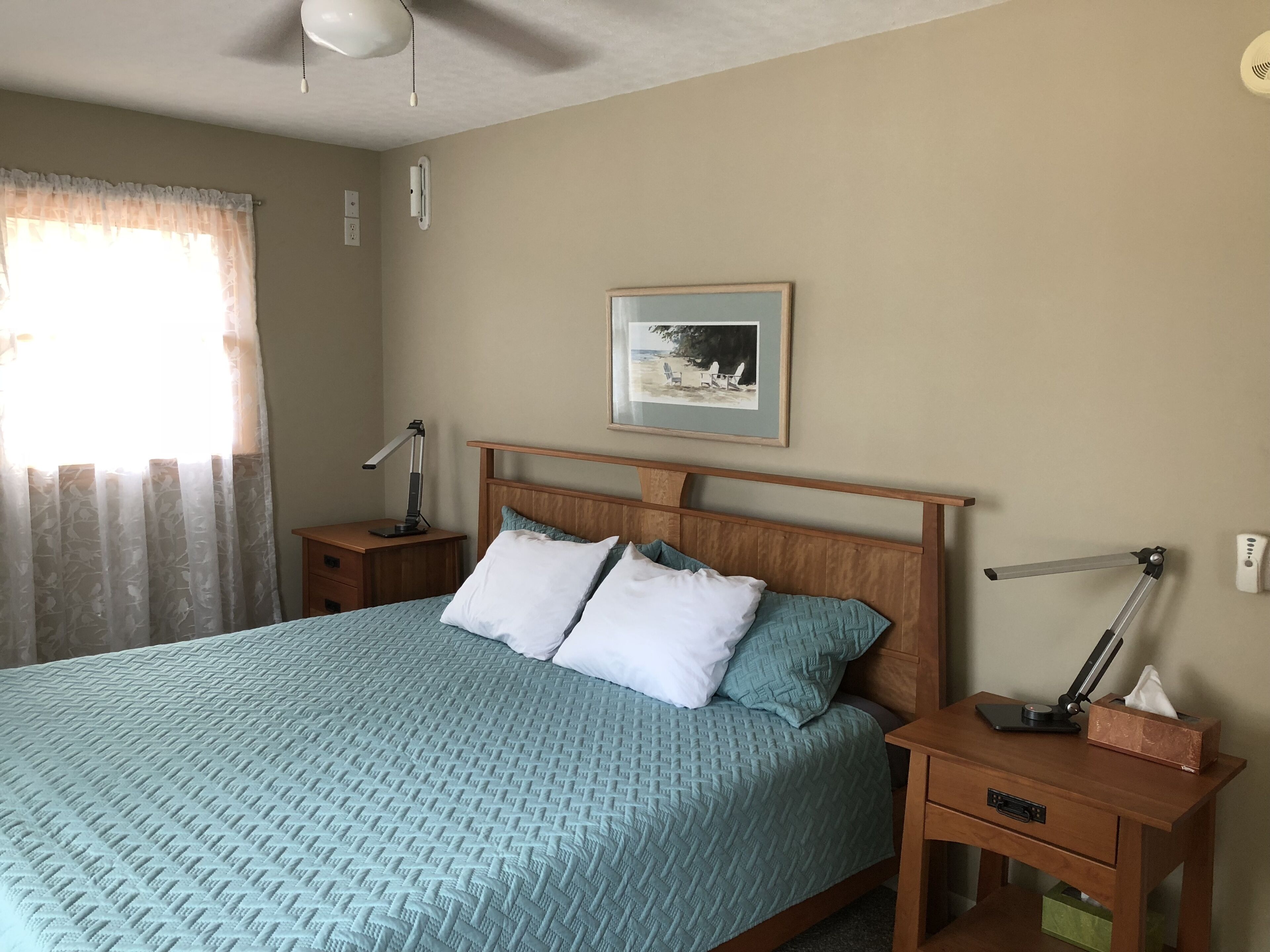 A neatly arranged bedroom with a bed, bedside tables, a desk, and a ceiling fan.