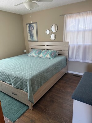 A bedroom with a bed, a ceiling fan, a window with curtains, and a wall-mounted mirror.
