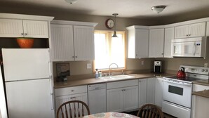 A kitchen with white cabinets, a sink, a stove, and a dining table with a patterned tablecloth.