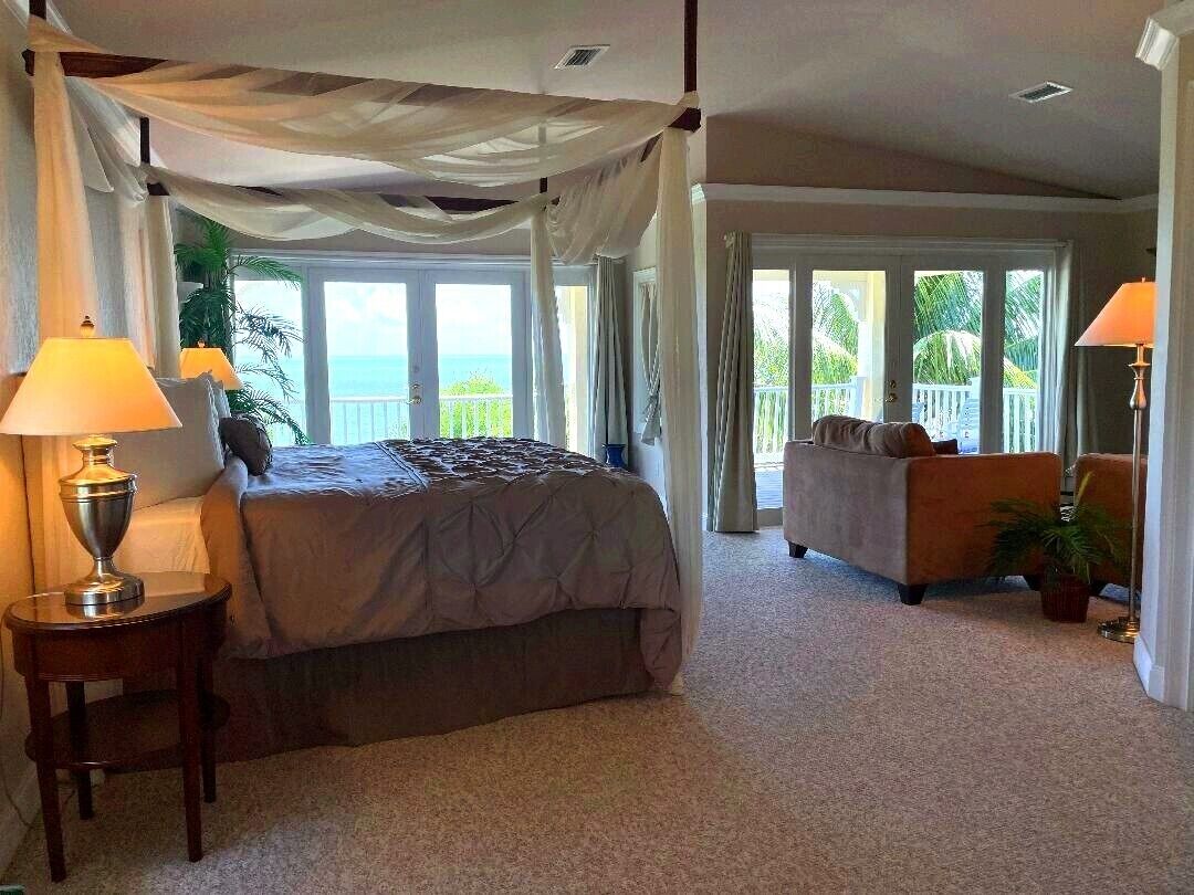 A bedroom with a canopy bed, a sitting area with a sofa, and a view of the ocean.