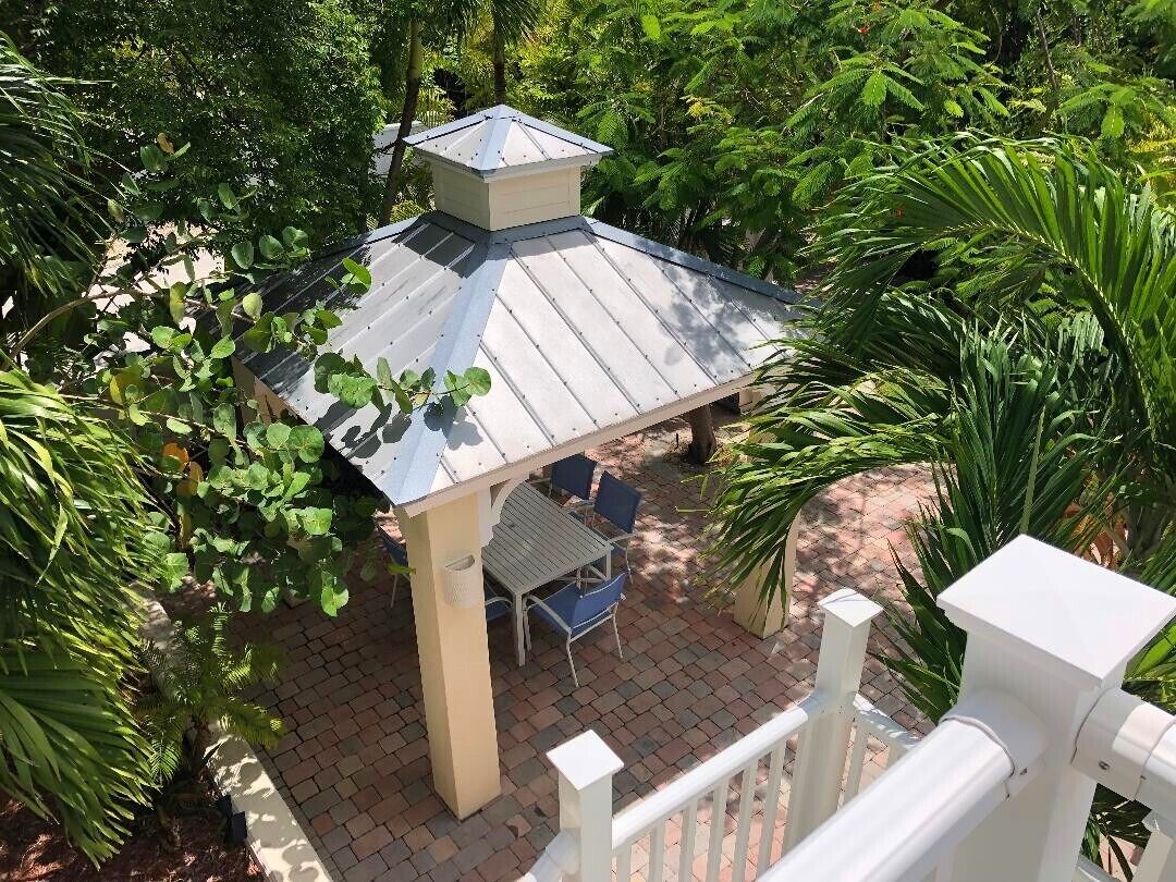 A covered patio area with a table and chairs, surrounded by lush greenery.