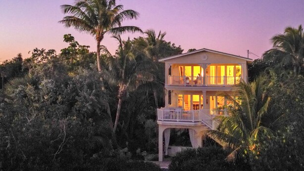 Una casa a due piani con un balcone, immersa in una fitta vegetazione tropicale.