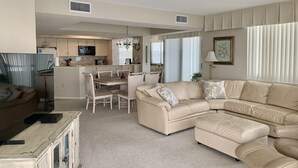 A spacious living room with a large beige sectional sofa, a dining area with a chandelier, and a kitchen with modern appliances. - Shoreham Towers II -  Corner Unit - Wrap-around Ocean Views (North Myrtle Beach)