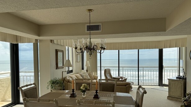 A spacious dining area with a large table and chairs, a chandelier, and a view of the ocean. - Shoreham Towers II -  Corner Unit - Wrap-around Ocean Views (North Myrtle Beach)
