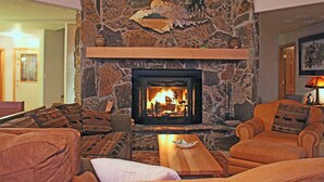 Une cheminée en pierre avec un feu, entourée d’un coin salon confortable avec des canapés et une table basse.