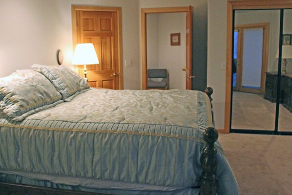 A bedroom with a bed, a lamp, a chair, and a door.