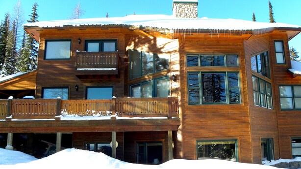 Une cabane en bois à plusieurs étages, dotée de balcons, de grandes fenêtres et d’un toit recouvert de neige.