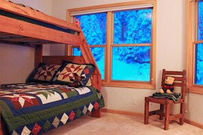 A bedroom with a bunk bed, a quilt, a chair, and a window with a view of trees.