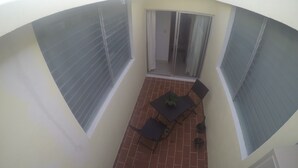 Eine kleine Terrasse mit Tisch, Stühlen und Topfpflanzen, sowie eine Glastür.