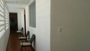 Ein Korridor mit an der Wand entlang gestellten Stühlen, einem Fenster mit Jalousien und einer Tür am Ende.