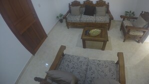 Ein Wohnzimmer mit einer Couch, einem Couchtisch und einem Sessel. Ein Fernseher ist an der Wand befestigt.