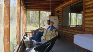 A cabin with a porch, wooden walls, and a bed with a checkered bedspread. - Bluebird cabin in Stanley, Idaho (Stanley)