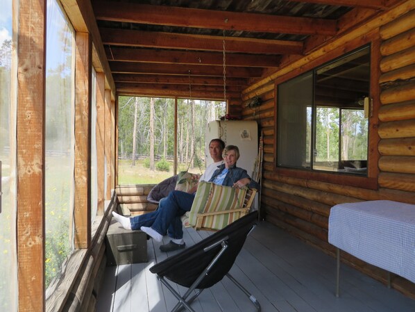 A cabin with a porch, wooden walls, and a bed with a checkered bedspread. - Bluebird cabin in Stanley, Idaho (Stanley)
