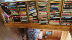 A wooden bookshelf filled with books, a bed with a floral bedspread, and a small window with a view of a wooden floor. - Bluebird cabin in Stanley, Idaho (Stanley)