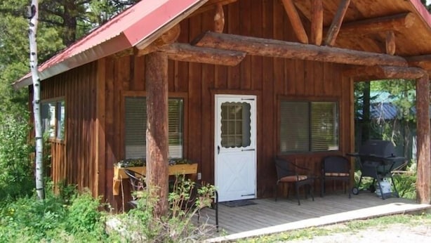 A wooden cabin with a porch, a door, and a grill area. - Cozy Cabin Minutes from Glacier's Two Medicine Valley (East Glacier)