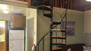 A compact living space with a spiral staircase, a refrigerator, a couch, and a painting on the wall. - Cozy Cabin Minutes from Glacier's Two Medicine Valley (East Glacier)