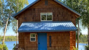 Eine Holzhütte mit blauer Tür, einem Metalldach und einem Steg, der zum See führt.