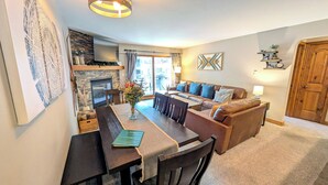 A cozy living room with a fireplace, a dining area with a table and chairs, and a sofa with cushions. - Luxury Condo w/ FREE WiFi, Parking, Heated Pool, Hot Tubs, Skier Shuttles (Avon)