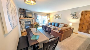 Una sala de estar acogedora con chimenea, un comedor con mesa y sillas, y un sofá con cojines.