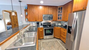 Una cocina moderna con armarios de madera, electrodomésticos de acero inoxidable, un lavamanos doble y un suelo estampado.