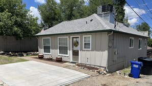 A single-story house with a grey roof, a front porch with potted plants, and a driveway. - The Cottage @ The Pleasant Street Suites in downtown Prescott (Prescott)