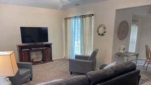 A living room with a flat-screen TV, a sofa, a chair, a lamp, and a small table with a decorative item. - The Cottage @ The Pleasant Street Suites in downtown Prescott (Prescott)