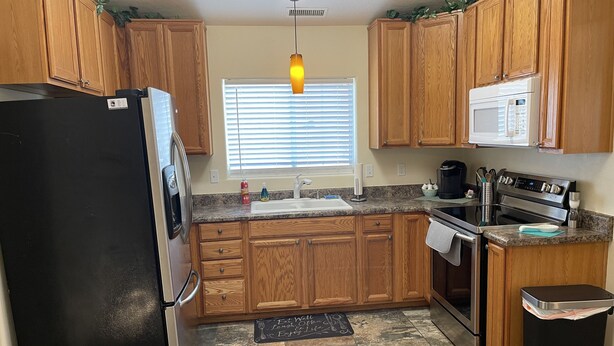 A compact kitchen with wooden cabinets, a black refrigerator, a microwave, a stove, and a sink. - The Cottage @ The Pleasant Street Suites in downtown Prescott (Prescott)