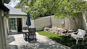 A backyard with a patio, a table, two chairs, a white bench, and a stone wall. - The Cottage @ The Pleasant Street Suites in downtown Prescott (Prescott)