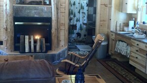 Interior acogedor de una cabaña con chimenea, paredes de madera, un comedor con mesa y sillas, y una cocina con armarios y fregadero.